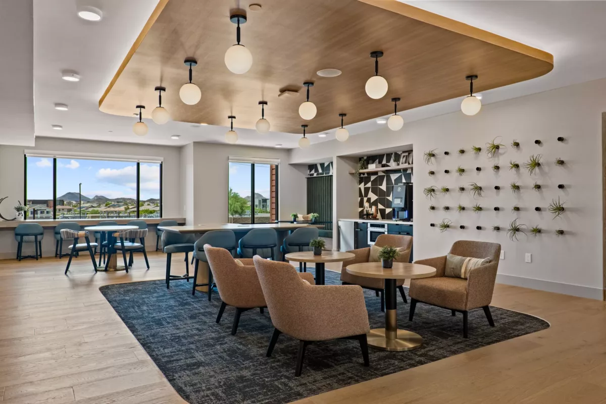 Lounge area with seating, tables, and a coffee bar. Large windows offer exterior views.