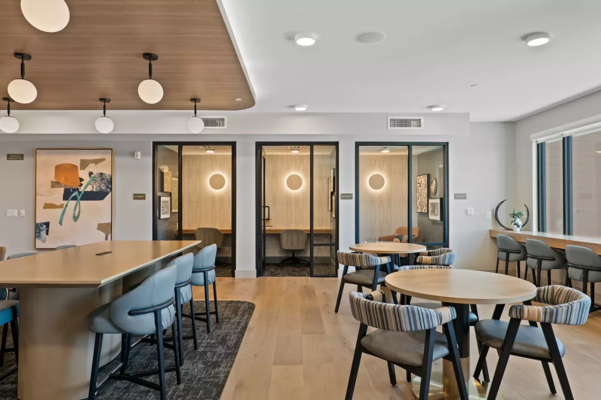Coworking space with tables, chairs, and three glass-enclosed office pods.