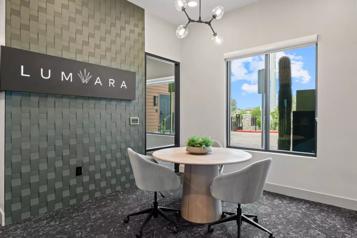 Modern meeting area with round table, chairs, and view of exterior landscaping. Textured wall.