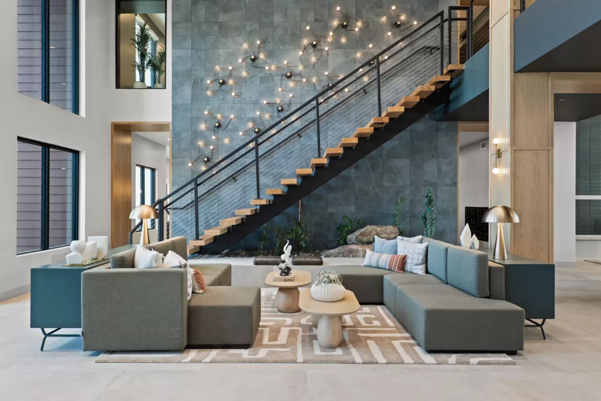 Modern lounge with gray sofas, wood stairs, and decorative wall lighting on a textured gray wall.