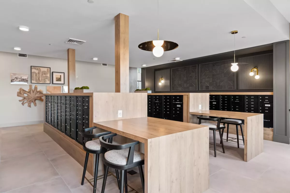 Mailroom with black mailboxes, wood desks, and chairs under modern pendant lighting.