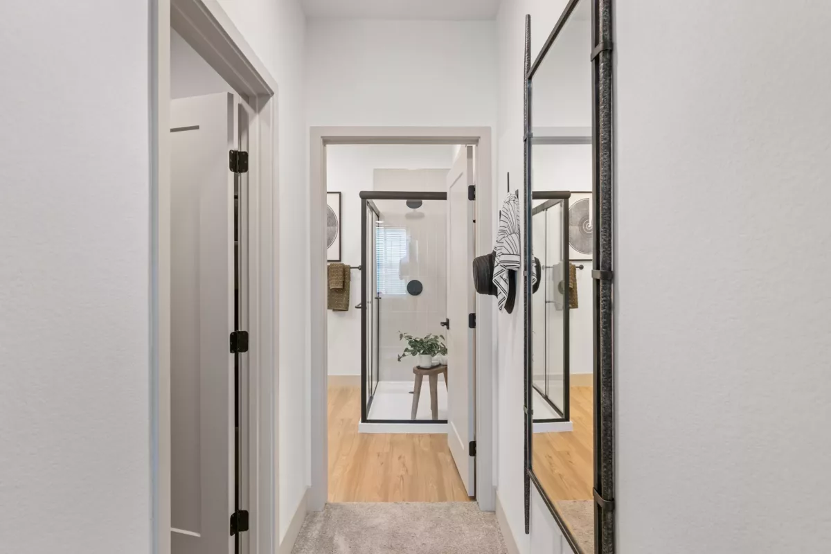Hallway view into bathroom with glass shower, wood floors, and decorative mirror.
