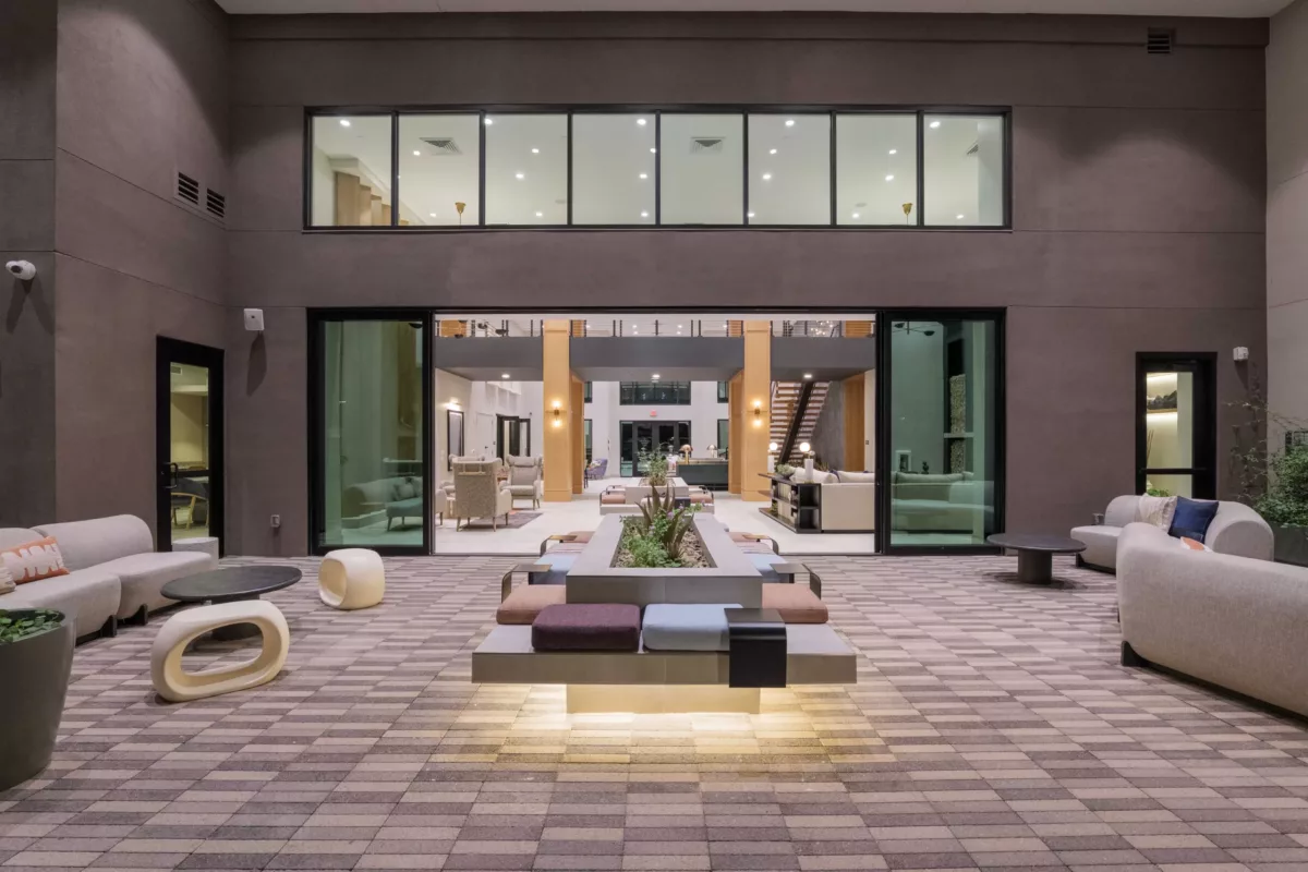 Indoor lounge area features modern seating, a central planter, and a view into another lounge space.