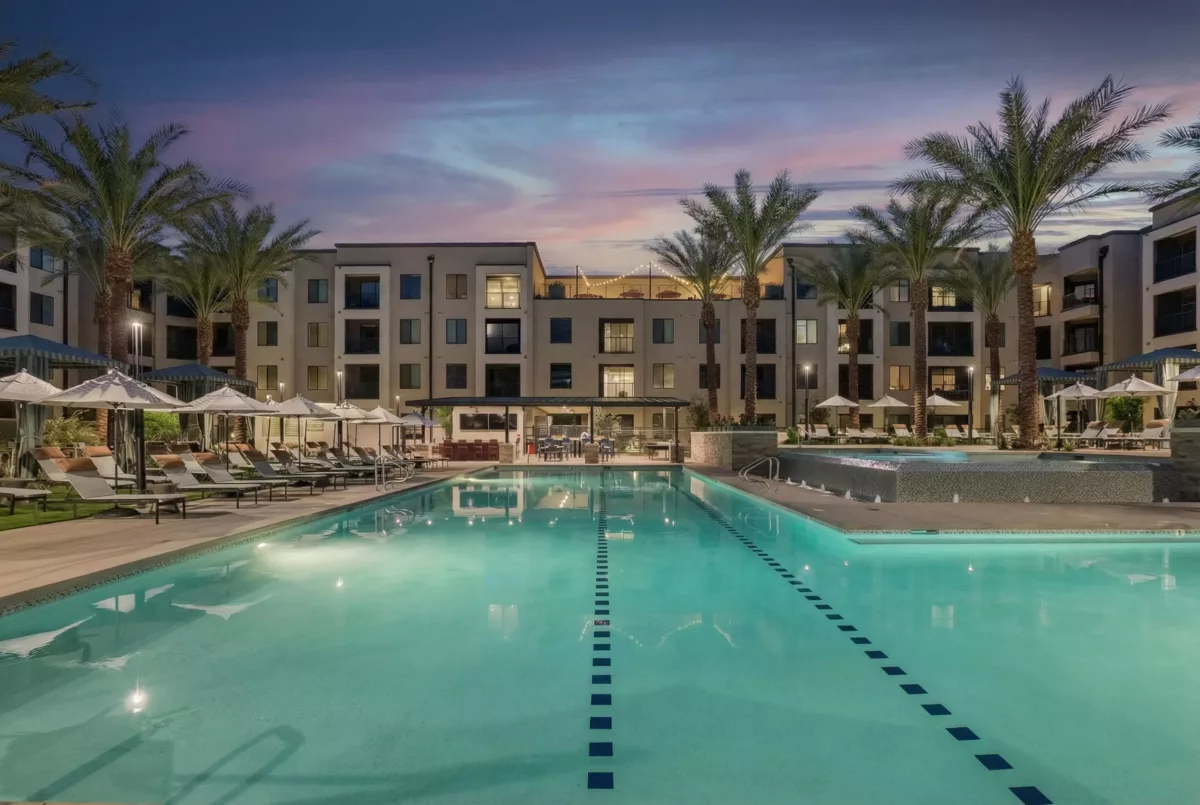 Large swimming pool with lounge chairs, cabanas, and a multi-story building in the background.