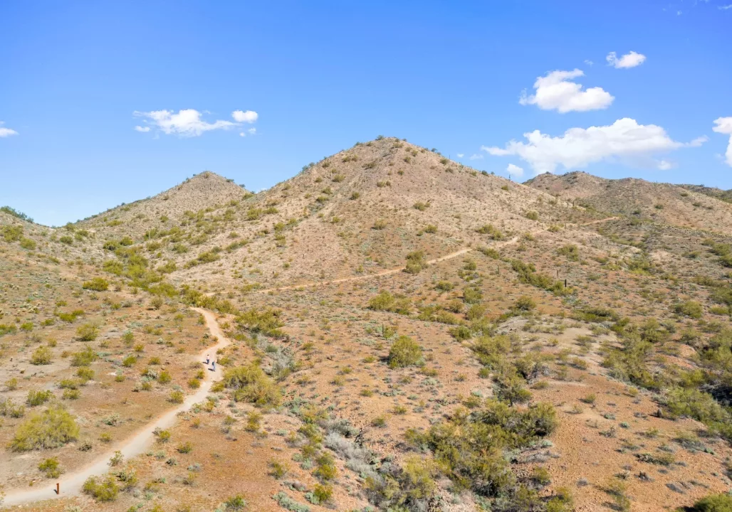 A scenic desert hiking trail winding through arid hills under a bright blue sky.