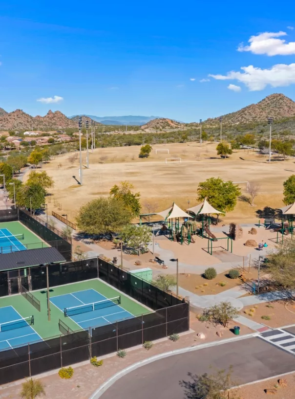 A community park featuring tennis courts, soccer fields, a playground, and mountain views.